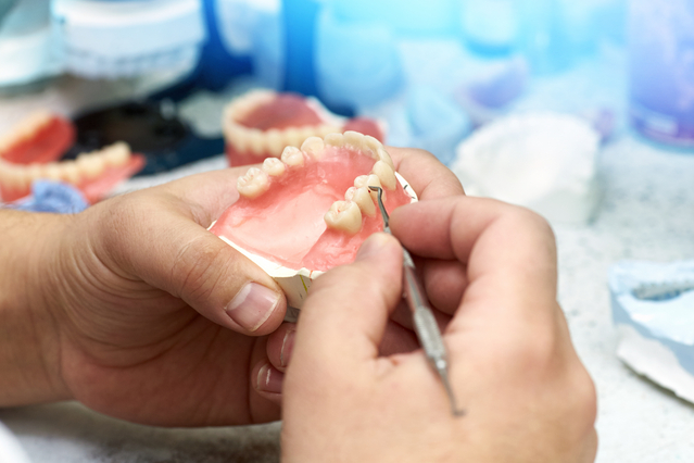 A dental technician working on a prosthetic care, meticulously shaping and adjusting a dental prosthesis.