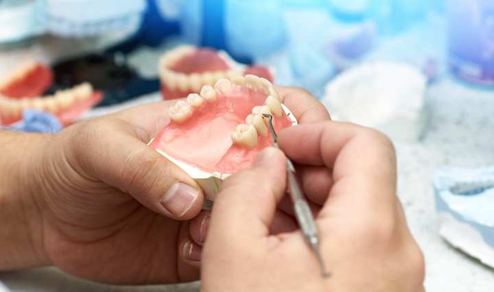 A dental technician working on a prosthetic care, meticulously shaping and adjusting a dental prosthesis.